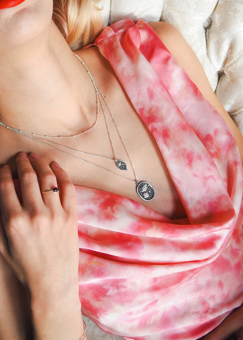 Woman wearing a pink and red patterned top with a necklace, lying on a bed.